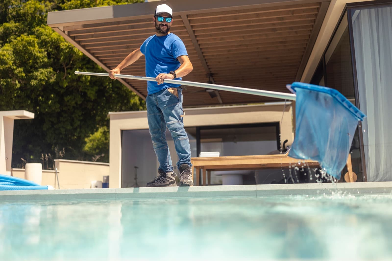 A pool professional working a net at the edge of a backyard pool